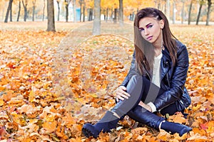 Beautiful girl in rock style with bright makeup in white jacket and black pants and boots in a leather jacket sitting in the Park