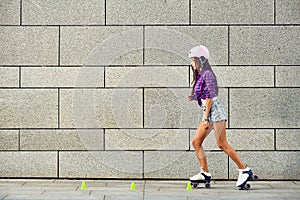 Beautiful girl rollerblading on the urban grey background in a park