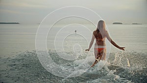 Beautiful girl runs on the water. Spray scattered. Slender young woman runs in the evening at sunset.