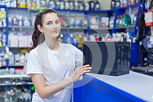 Beautiful girl saleswoman offers the best battery for car in an auto parts store