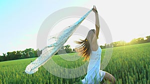 Beautiful girl with scarf flying in wind running on wheat field in sunset. Freedom beayty health happiness concept