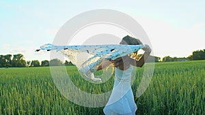 Beautiful girl with scarf flying in wind running on wheat field in sunset. Freedom beayty health happiness concept