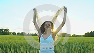 Beautiful girl with scarf flying in wind running on wheat field in sunset. Freedom beayty health happiness concept