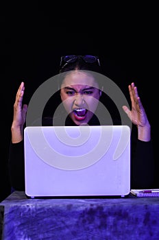 Beautiful girl screaming in front of her laptop on dark background