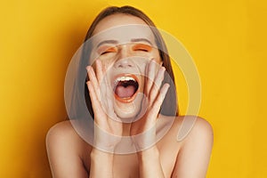 Beautiful girl with shiny brown straight long hair. Woman with orange makeup with freckles. Girl eyes closed screaming .