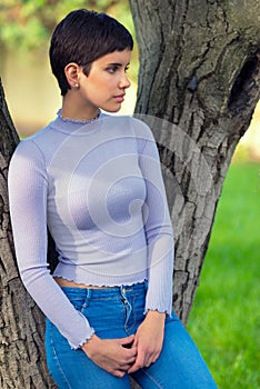 Beautiful girl with short hair resting beside tree in spring