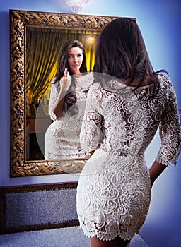 The beautiful girl in a short white dress looking into mirror