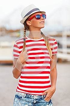Beautiful girl in shorts and striped t-shirt, in sunglasses, in hat, outdoors. Tanned woman in summer