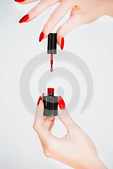 Beautiful girl showing red manicure nails. red nail polish bottle on white background. Stylish trendy female manicure.