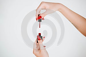 Beautiful girl showing red manicure nails. red nail polish bottle on white background. Stylish trendy female manicure.