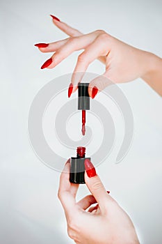 Beautiful girl showing red manicure nails. red nail polish bottle on white background. Stylish trendy female manicure.