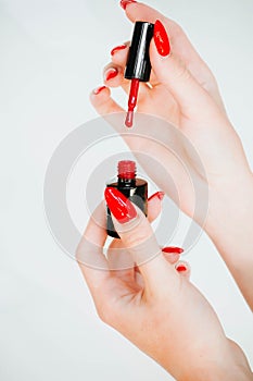 Beautiful girl showing red manicure nails. red nail polish bottle on white background. Stylish trendy female manicure.