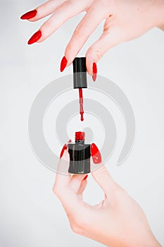 Beautiful girl showing red manicure nails. red nail polish bottle on white background. Stylish trendy female manicure.