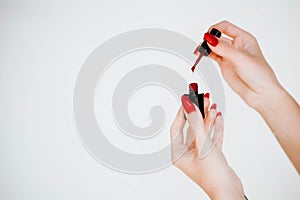 Beautiful girl showing red manicure nails. red nail polish bottle on white background. Stylish trendy female manicure.