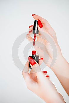 Beautiful girl showing red manicure nails. red nail polish bottle on white background. Stylish trendy female manicure.