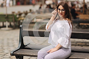 Beautiful girl sits on benth in centre of city. She relaxes and waits for her husband
