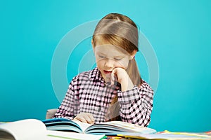 Beautiful girl sits at dchool desk, puts her hand in chin, attentively and enthusiastically reads the book aloud on blue