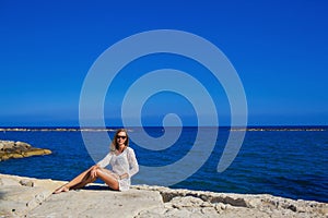 A beautiful girl sits on the rocky shore of the Mediterranean Sea Cyprus.