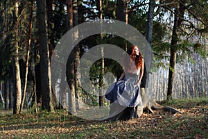 Beautiful girl sits on stump in autumn forest