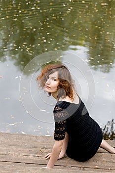 Beautiful girl sitting on bank of a pond