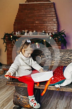 A beautiful girl is sitting on a bench and opens a box with a Christmas gift. The concept of Christmas and New Year, on