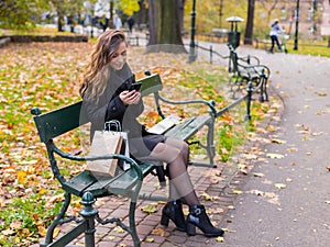 Beautiful girl sitting on a bench, woman with your phone writes a message on social networks, sunny autumn day in the park, woman