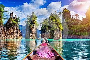 Beautiful girl sitting on the boat and looking to mountains in Ratchaprapha Dam at Khao Sok National Park, Surat Thani Province photo