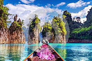 Beautiful girl sitting on the boat and looking to mountains in Ratchaprapha Dam at Khao Sok National Park, Surat Thani Province