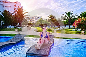 Beautiful girl sitting on deckchair. Sunset by the pool near the hotel, arab tropical evening