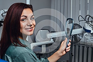 Beautiful girl sitting in a dentist chair with mirror in hands, looking at camera.