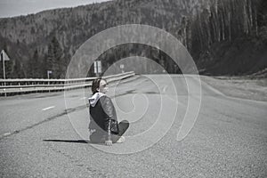 A beautiful girl is sitting on an empty road.