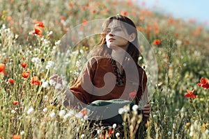 Beautiful girl sitting in the grass and poppies