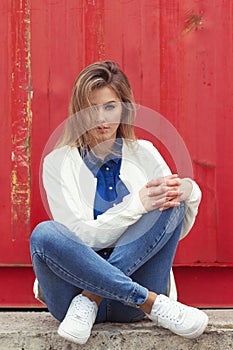 Beautiful girl sitting on the ground near the wall in jeans and a white blouse , her hair develops wind