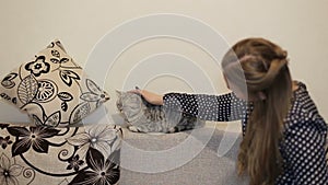 Beautiful girl sitting in living room at home and stroking a cat