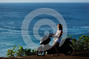 Beautiful girl sitting on a motorcycle on a cliff