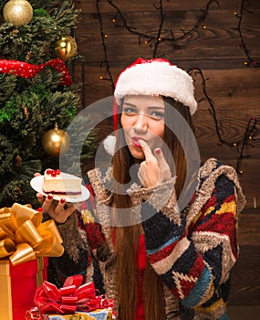 Beautiful girl sitting near New Year tree and eating delicious cake