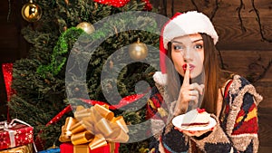 Beautiful girl sitting near New Year tree and eating delicious cake