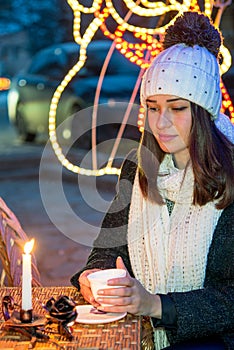 beautiful girl sitting outdoors in winter with a cup and a candle