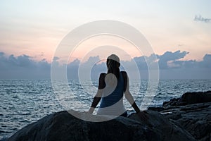 The beautiful girl sitting on stones and looking in a distance, the girl at sunset to meditate in silence, beautiful body. concept