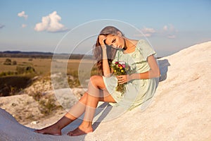 Beautiful girl sitting on white hills on the sunset. Pretty suntanned girl with bouquet of flowers sitting on mountains with amazi