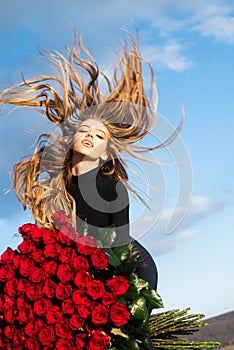 Beautiful girl on sky background. Girl and roses. Favorite flowers. Gift with love. Happy girl hugs a bouquet. Valentine
