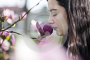 Beautiful girl smelling the flowers. Blossoming magnolia in the park garden.