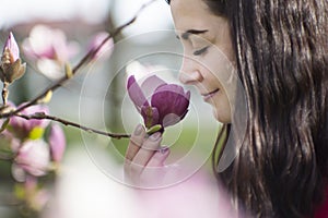 Beautiful girl smelling the flowers. Blossoming magnolia in the park garden.