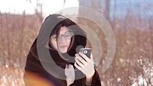 Beautiful girl in a snow-covered winter city using Skype on a smartphone communicates with his family