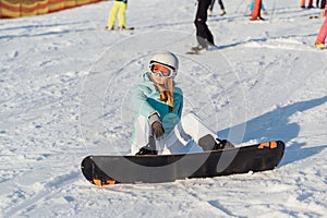 A beautiful girl snowboarder sits on a slope, resting after a difficult descent