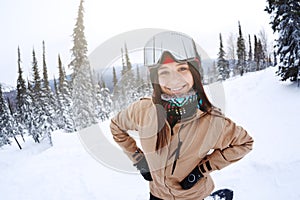 Beautiful girl snowboarder smiling, looking at the camera, around the snowy forest of the ski resort