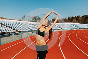 Beautiful girl in sportswear standing on the running track and preparing to run. Morning warm-up before exercise.