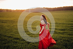 A beautiful girl in spring in a red dress is walking in a field at sunset. Taken from the air by a quadrocopter