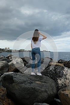 Beautiful girl standing on beach rocks looking to the sea