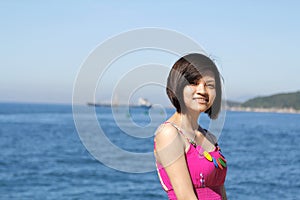 A beautiful girl is standing besides the beach with blue sea and cloud sky